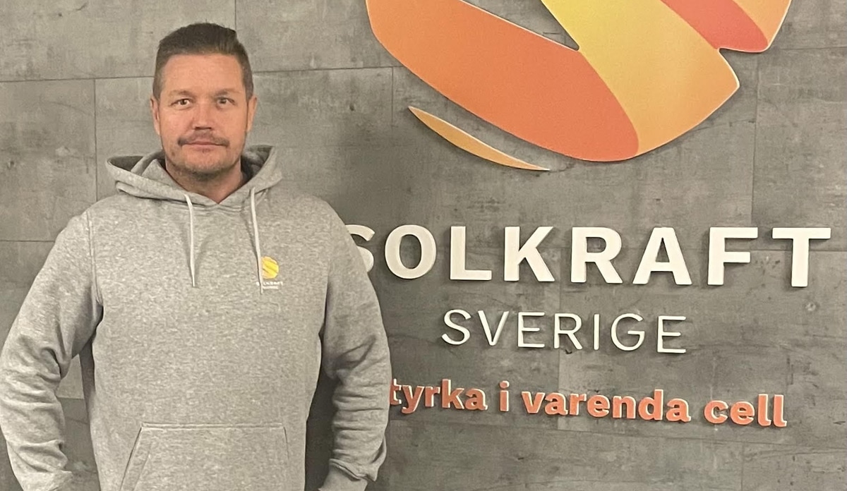 Urban Aheinen som jobbar på Solkraft Sverige står framför en grå vägg. På väggen syns företagets logotyp och slogan. Urban har en grå hoodie med Solkraft-logga på sig.